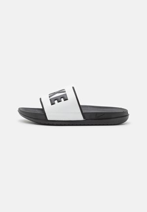 Sandale Nike slide noire et blanche avec une large bride blanche arborant un lettrage Nike noir en gras et une semelle noire rembourrée.