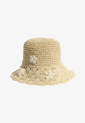 Beżowy, szydełkowany kapelusz typu bucket z szerokim rondem, ozdobiony pięcioma małymi białymi muszlami w kształcie kwiatów.