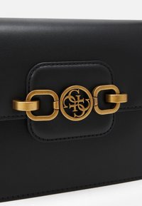 Černé kožené psaníčko s kovovým zlatým řetízkem a zapínáním s logem, hladká textura, obdélníkový tvar s detailním prošíváním.