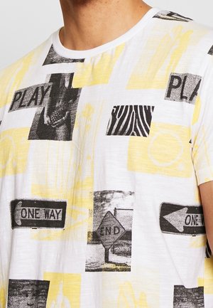Short-sleeve t-shirt made of soft fabric, featuring a white base with yellow and black graphic prints, including traffic signs and animal patterns.