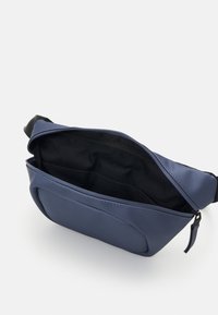 Σακίδιο μέσης σε ναυτικό μπλε χρώμα με λεία υφή, ρυθμιζόμενη ζώνη και φερμουάρ που αποκαλύπτει ένα μαύρο εσωτερικό ύφασμα με τσέπες.