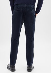 Marynarski sztruksowe spodnie o fakturowanej powierzchni, z elastycznym paskiem i dwoma tylnymi kieszeniami. Noszone z czarnymi butami, prezentujące prostą nogawkę.