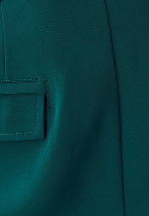 Mėlynas audinys su šoniniu kišenėmis, lygiu tekstūru ir vienodu paviršiumi, matomomis siūlių detalėmis aplink kišenės angą.