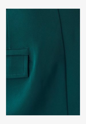 Teal tkanina z bočno našitim žepom, gladka tekstura in enakomerna površina z vidnimi šivi okoli odprtine žepa.