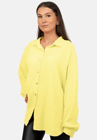 Camicia a pulsante di colore giallo brillante, realizzata in tessuto texturizzato. Presenta un colletto, maniche lunghe e una vestibilità comoda.