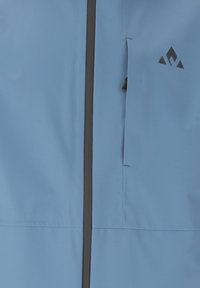 Ljusblå jacka med dragkedja framtill och svart dragkedja, sidoficka och en logotyp på övre vänstra sidan. Slät, vattentålig material.