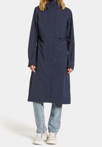 Imperméable bleu marine avec un col montant, des manches longues, des poches avant et une coupe décontractée. Associé à un jean bleu clair et des baskets neutres.