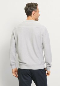 Grauer Pullover mit langen Ärmeln, gerippten Bündchen und Taillenbund. Geschmeidige Textur, Rundhalsausschnitt-Design, minimale Nähtdetails auf der Rückseite.