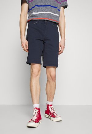 Bermuda blu navy realizzati in misto cotone, slim fit con passanti per la cintura, tasche frontali e orlo al di sopra del ginocchio. Abbinati a sneakers rosse alte.