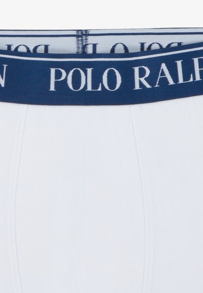 Valged bokserpüksid tumesinise elastse vöökohaga, mille peal on valgete tähtedega kiri "POLO RALPH". Kangas tundub pehme ja veniv.