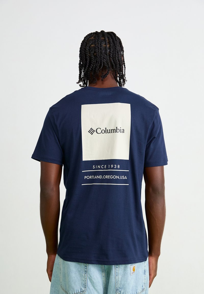Marineblå bomulds T-shirt med et stort hvidt firkantet grafisk print med "Columbia" logo, “SINCE 1938,” og teksten “PORTLAND, OREGON, USA.”