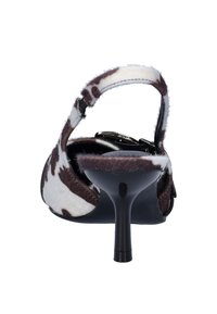 Back view of a heeled shoe featuring a cowhide pattern in white and brown, with a slender heel and an adjustable ankle strap.