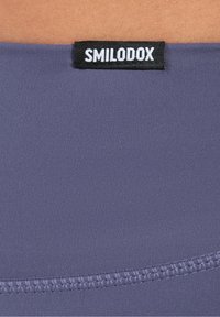 Leggings grigio-viola con un tessuto liscio e testurizzato, dotati di un'etichetta nera con la scritta "SMILODOX" sulla vita.