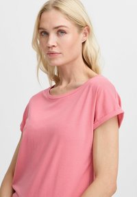 T-shirt rose à manches courtes en tissu doux, avec un col rond et des manches retroussées, au toucher lisse et à la coupe décontractée.
