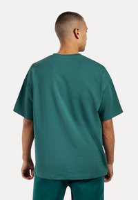 Turkusowa bawełniana koszulka z luźnym krojem, krótkimi rękawami i klasycznym okrągłym dekoltem, zaprezentowana z tyłu na modelce.