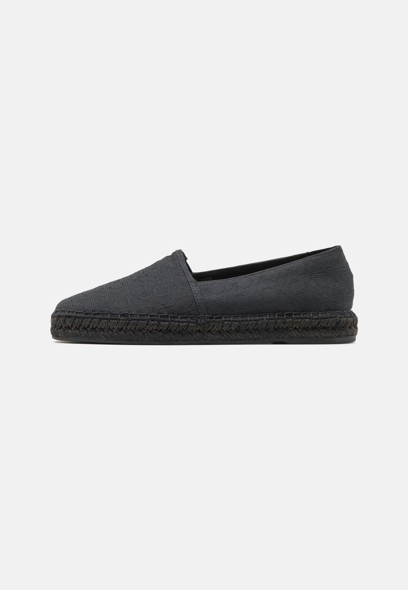 Espadrille noire à enfiler avec tissu texturé, bout rond et semelle en jute tressé. Design minimaliste sans matériel visible.