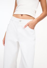 Weiße hoch taillierte weit geschnittene Jeans aus Denim, mit Vordertaschen und einem silbernen Knopfverschluss sowie minimalen Nähdetails.