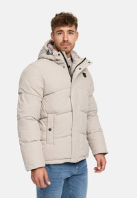 Lys beige pufferjakke med hætte, der har lynlås, trykknapper og sidelommer. Tyk polstring og quiltet design.