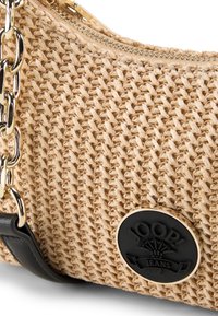 Beżowa torebka z tkaniny o plecionym wzorze, z zamknięciem na zamek, złotym łańcuszkiem na ramię i okrągłym czarnym logo. Gładka tekstura z wyrafinowanymi detalami.
