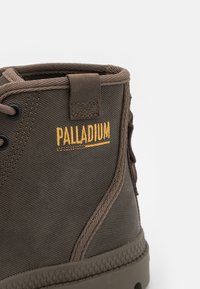 Pruunist kanvasest pahkluu saapad tekstureeritud pinnaga, pruuni nööridega ja tan värvi "PALLADIUM" logoga. Omab kummist tallat ja õmmeldud aktsente.