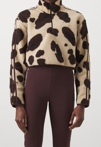 Klippt fleece-pullover i beige med bruna fläckar, hög krage och halv dragkedja fram. Matchas med bruna figurnära leggings med sidosträck.