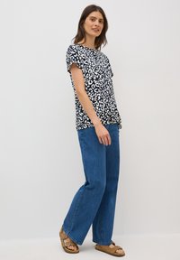 Mörkblå topp med vit leopardtryck, korta ärmar och lös passform, tillsammans med ljusblå vida jeans och stängda sandaler.