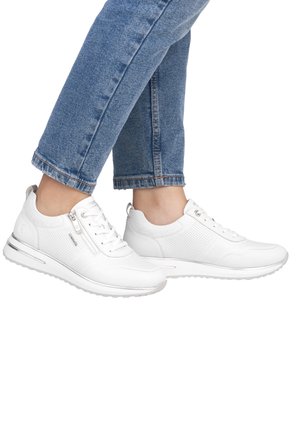 White athletic sneakers with a textured upper, laces, side zip, and a cushioned sole. Worn with cropped blue denim jeans.