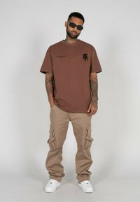 Brun crewneck t-shirt med sort grafik på brystet, parret med beige cargo bukser med sidelommer og hvide sneakers.