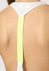 Acercamiento a la parte superior de la espalda de una persona que lleva una prenda blanca con una tira vertical de color amarillo pálido que recorre la columna vertebral.