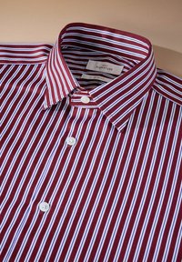 Schlankes Hemd mit rot-weißen Streifen und Button-Down-Kragen, ausgestattet mit weißen Knöpfen und einer glatten Stofftextur. Etikett im Kragen sichtbar.