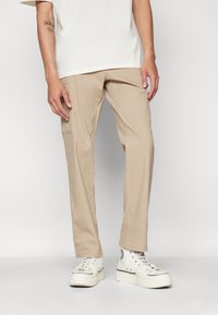 Beige cargobroek met zijzakken, rechte snit, van katoen gemaakt en met een gladde textuur, gecombineerd met witte hoge sneakers.