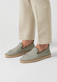 Zapatos slip-on tipo espadrilla con un patrón de cuadros verde y blanco, suela de yute y acentos verdes en el borde. Parte superior de textil tejido.