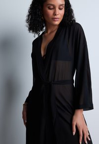 Kimono noir transparent avec de longues manches, un design enveloppant et une taille nouée. Texture lisse, transparence subtile et style minimaliste.