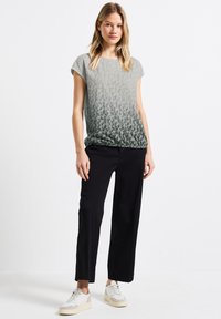 T-shirt gris dégradé avec un motif subtil de léopard, associé à un pantalon noir à jambes larges et des baskets blanches. Design simple, coupe décontractée.