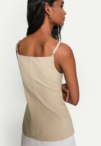 Beige ribbad topp med tunna justerbara band, fyrkantig halsringning och subtila vertikala linjer, med en figurnära design.