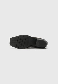 Suola di scarpa in gomma nera con motivo di grip testurizzato e branding. Forma arrotondata con bordo liscio, progettata per resistenza e trazione.