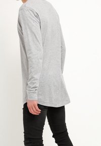 Långärmad grå t-shirt med rund halsringning och sidosprund, i kombination med svarta slim-fit byxor. Bomullstyg, slät textur.