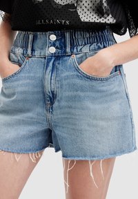 Shorts de mezclilla en azul claro con cinturilla elástica, cierre de dos botones, bolsillos frontales y dobladillo deshilachado. Textura suave con áreas descoloridas.