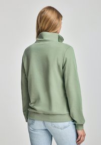 Grön sweatshirt med hög krage, gjord av mjukt tyg. Har en avslappnad passform och ribbade muddar. Kombineras med ljusa denimjeans.