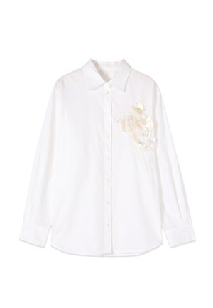Witte blouse met lange mouwen, knopen en een puntige kraag, met decoratieve witte bloemenapplicaties op de linkerborst.