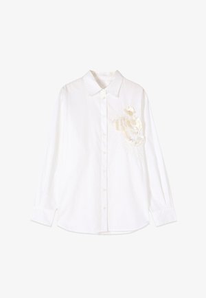 Valkoinen pitkähihainen napillinen kauluspaita, jossa on terävä kaulus ja koristeellinen valkoinen kukkakuvio vasemmassa rinnassa.