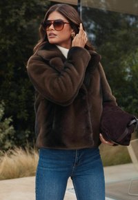 Pruuni faux nahast jakk kõrge kraega, koos kreemika särgiga ja tumehallide teksadega. Pruun sametist kott ja ülepaisutatud prillid lisatud.