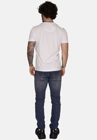 T-shirt bianco a maniche corte e jeans blu scuro indossati da una figura maschile, con una vestibilità dritta e una texture denim classica. Sneakers nere completano il look.