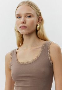 Barna bordázott ujjatlan felső, csipke díszítéssel a nyakvonalon és a karöltőknél, testhezálló fazonban és puha tapintású anyagból. Arany karika fülbevalók a háttérben.