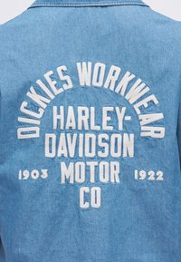 Μπλε τζιν μπουφάν από πίσω με λευκό κεντητό κείμενο: "DICKIES WORKWEAR HARLEY-DAVIDSON MOTOR CO 1903 1922."