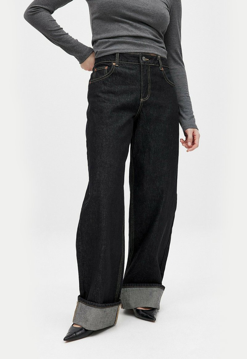 Svarta vida jeans med hög midja, kontrasterande gula sömmar och uppvikt midja i grå denim. Har framfickor och knäppning.