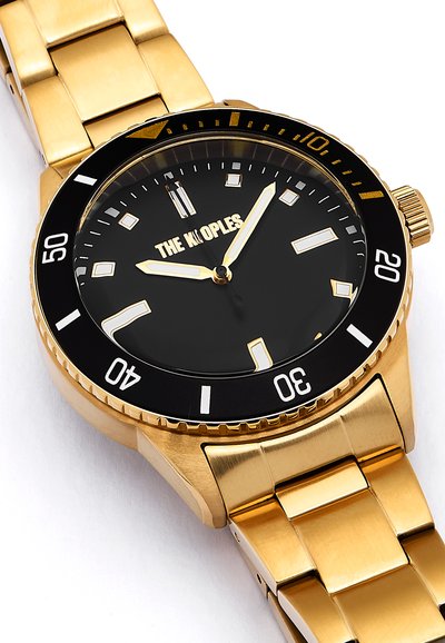 Reloj de metal dorado con esfera negra, grandes índices plateados y tres manecillas. Presenta un bisel unidireccional con marcadores blancos y una pulsera de eslabones.