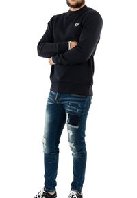 Felpa in cotone blu marina con polsini e collo a costine. Indossata con jeans blu scuri strappati caratterizzati da una macchia scura e sneakers con dettagli bianchi.