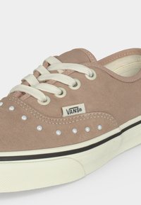 Μπεζ Vans low-top αθλητικό παπούτσι με λευκά κορδόνια, λευκά σημεία στη πλευρά και λευκή λαστιχένια σόλα με μαύρη ρίγα.