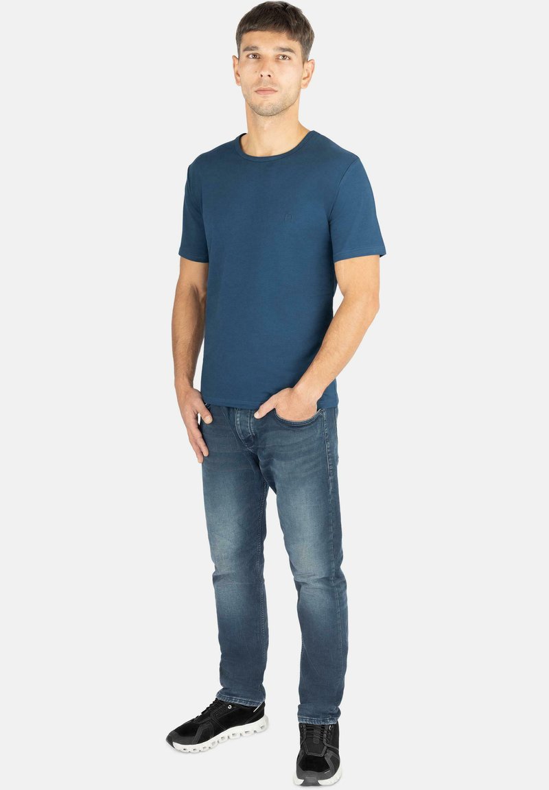 Marineblaues T-Shirt mit kurzen Ärmeln und Rundhalsausschnitt, kombiniert mit hellblauen Jeans und schwarzen Sneakers mit weißen Sohlen.